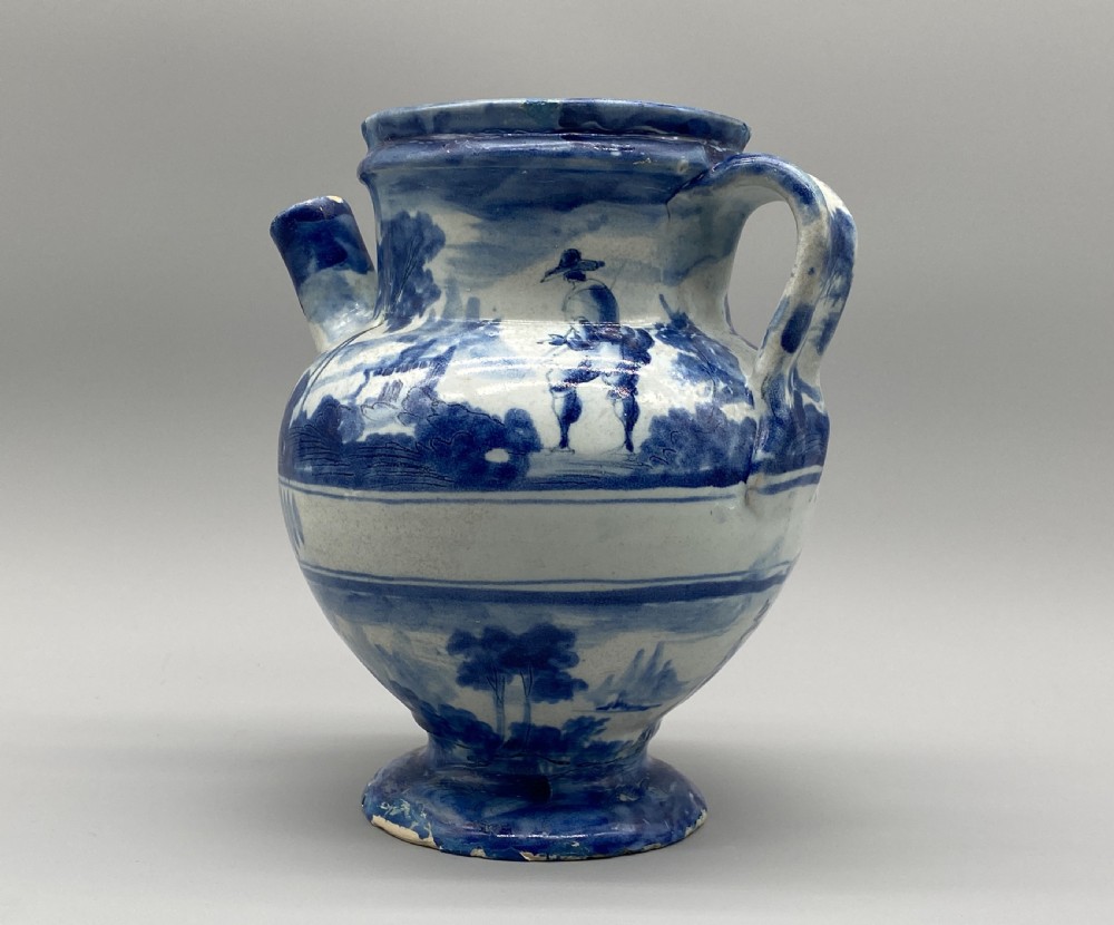 An 18th-century Italian Savona majolica wet drug jar featuring hand-painted cobalt blue landscapes, a single side handle, a raised spout, and a pedestal base. View V