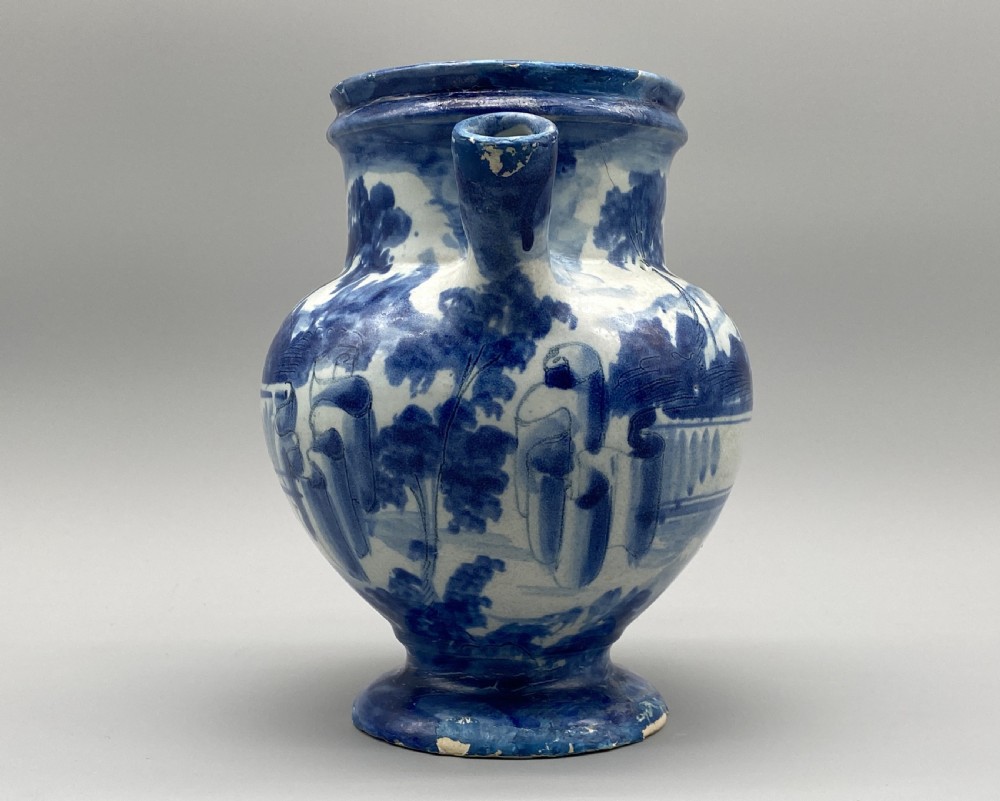 An 18th-century Italian Savona majolica wet drug jar featuring hand-painted cobalt blue landscapes, a single side handle, a raised spout, and a pedestal base. View VII