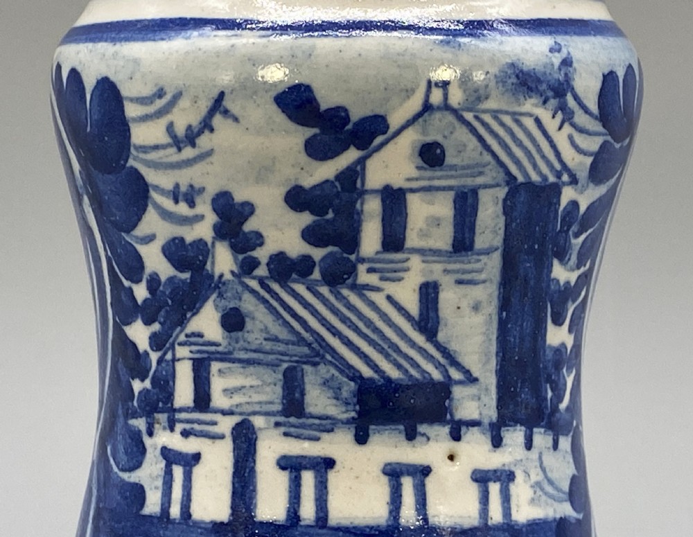A cylindrical tin-glazed earthenware albarello jar with a waisted body featuring hand-painted blue scrollwork and the date 1709 on a cream-white background. View VII