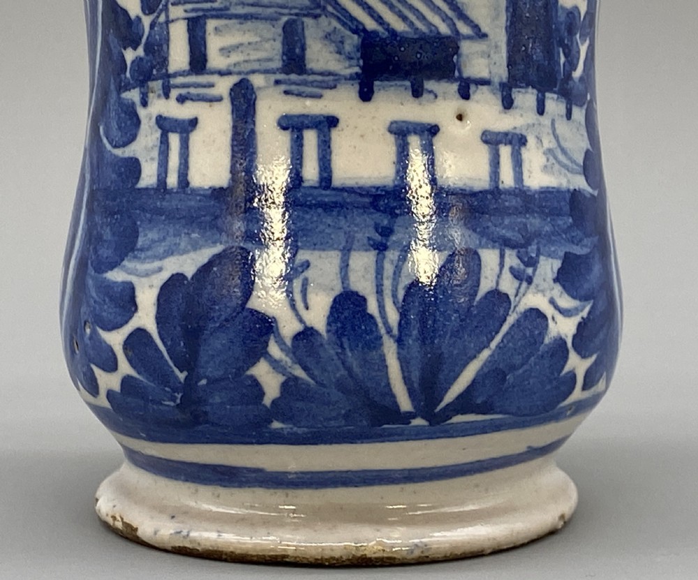 A cylindrical tin-glazed earthenware albarello jar with a waisted body featuring hand-painted blue scrollwork and the date 1709 on a cream-white background. View VIII