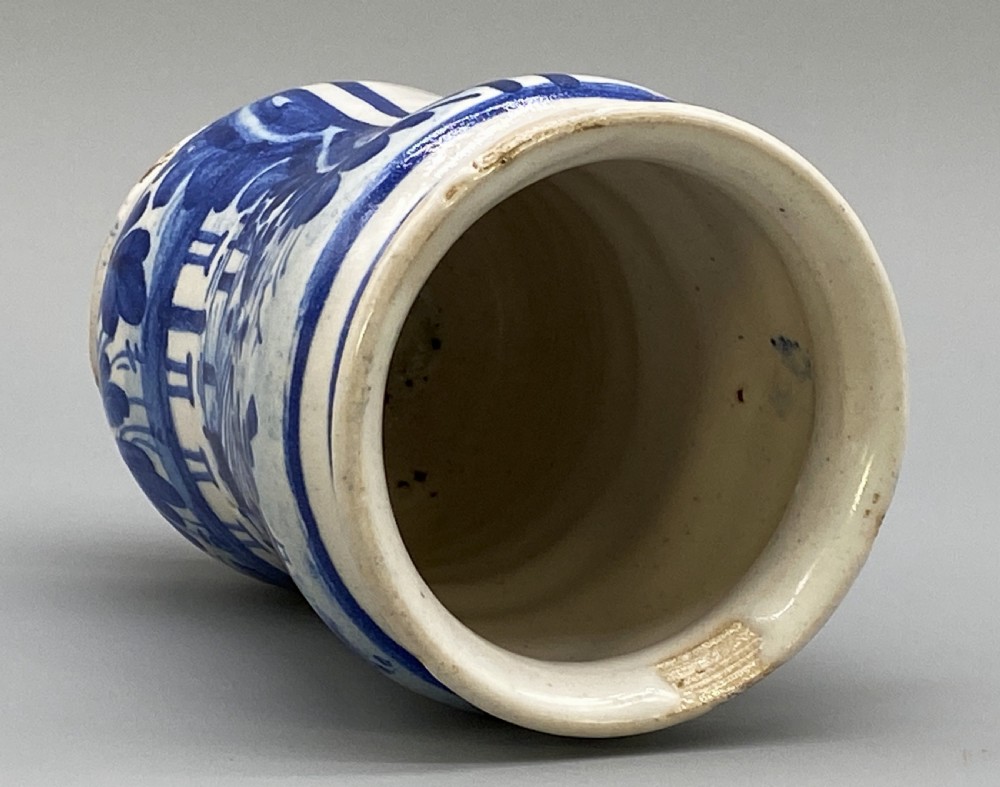 A cylindrical tin-glazed earthenware albarello jar with a waisted body featuring hand-painted blue scrollwork and the date 1709 on a cream-white background. View IX