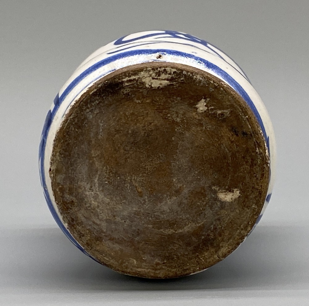 A cylindrical tin-glazed earthenware albarello jar with a waisted body featuring hand-painted blue scrollwork and the date 1709 on a cream-white background. View XI
