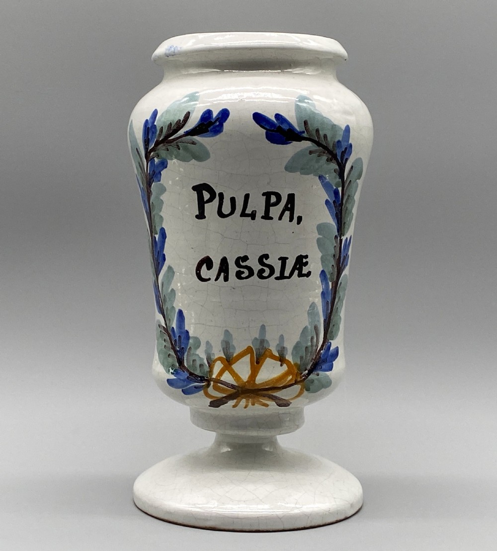 A pair of white tin-glazed ceramic albarello apothecary jars featuring hand-painted green foliage wreaths and Latin script on pedestal bases. View X