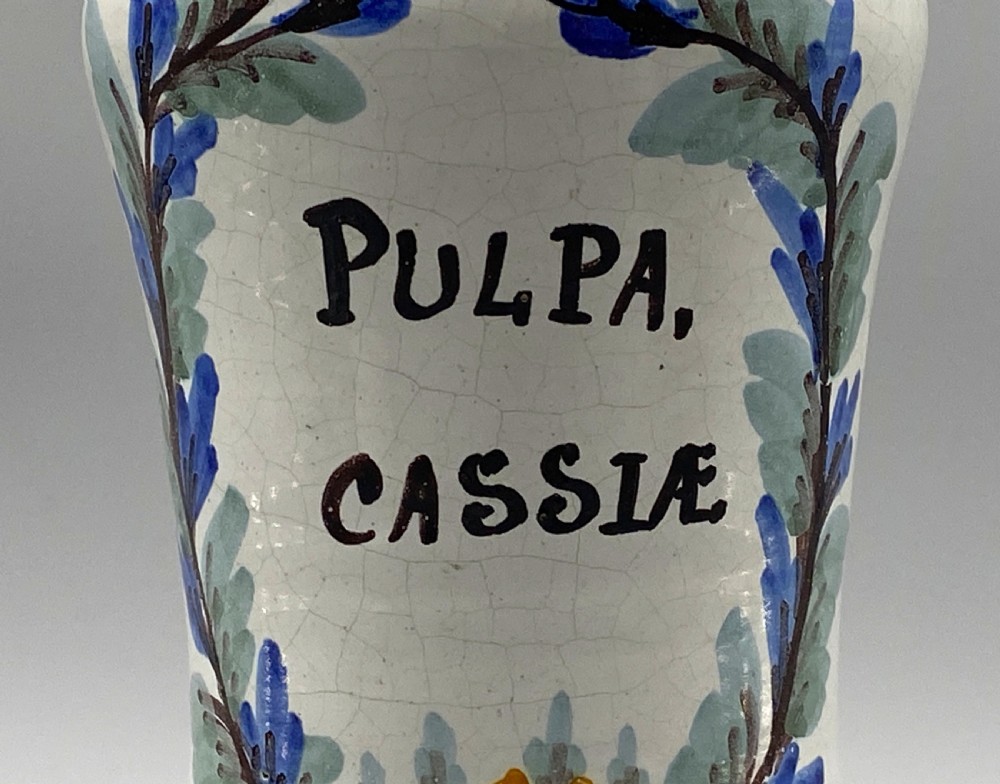 A pair of white tin-glazed ceramic albarello apothecary jars featuring hand-painted green foliage wreaths and Latin script on pedestal bases. View XII