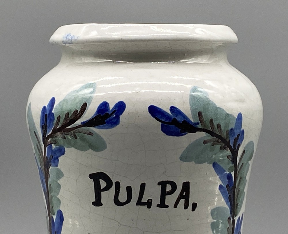 A pair of white tin-glazed ceramic albarello apothecary jars featuring hand-painted green foliage wreaths and Latin script on pedestal bases. View XIII