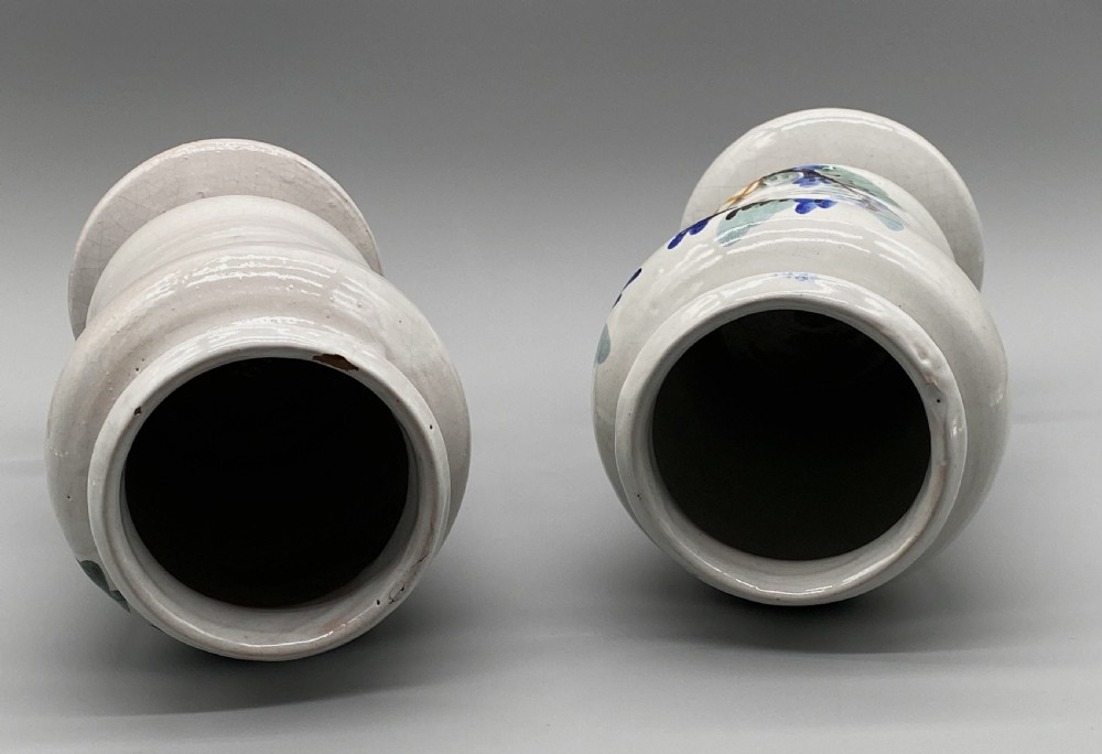 A pair of white tin-glazed ceramic albarello apothecary jars featuring hand-painted green foliage wreaths and Latin script on pedestal bases. View XVI