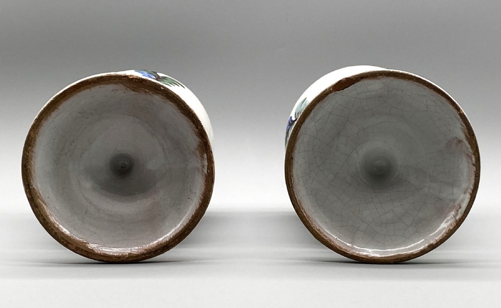 A pair of white tin-glazed ceramic albarello apothecary jars featuring hand-painted green foliage wreaths and Latin script on pedestal bases. View XVII