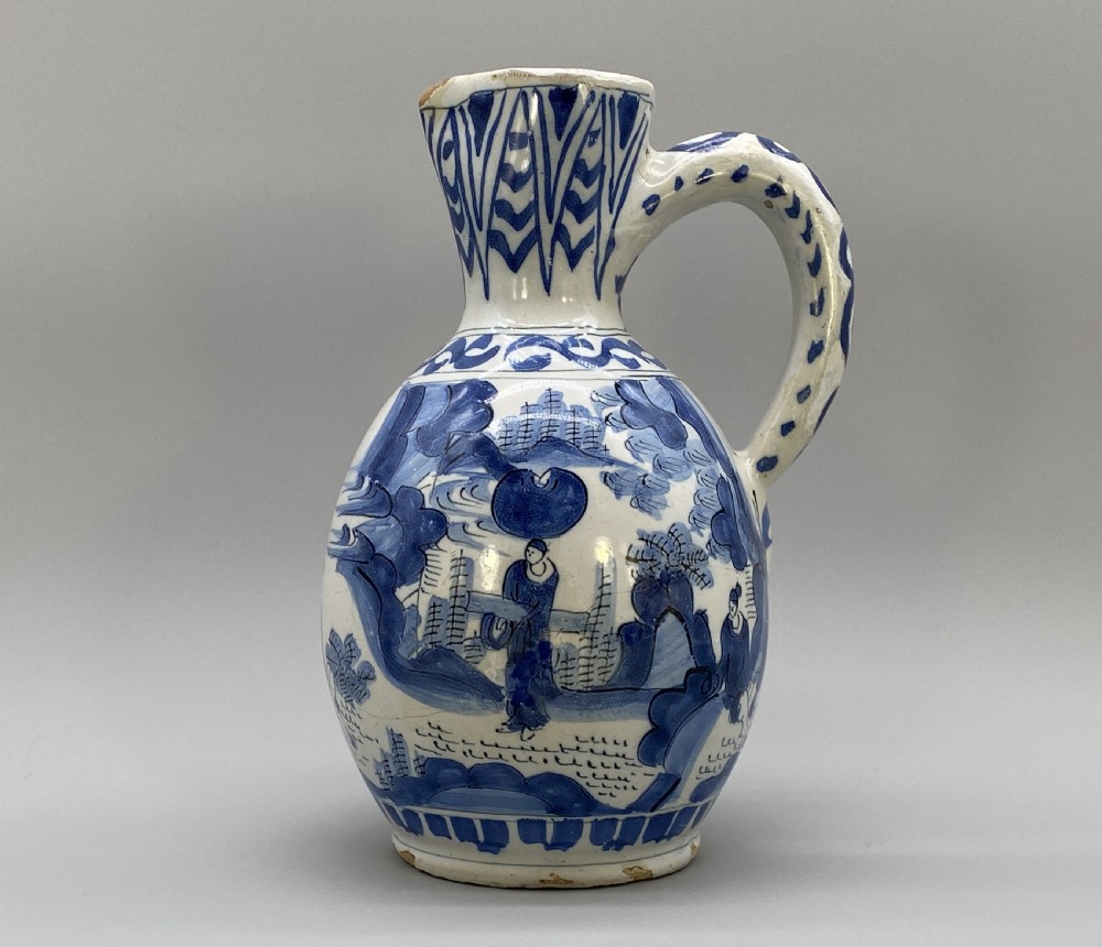 A 17th-century Dutch Delftware ceramic jug featuring hand-painted blue chinoiserie scenes on an opaque white tin glaze with a curved handle.