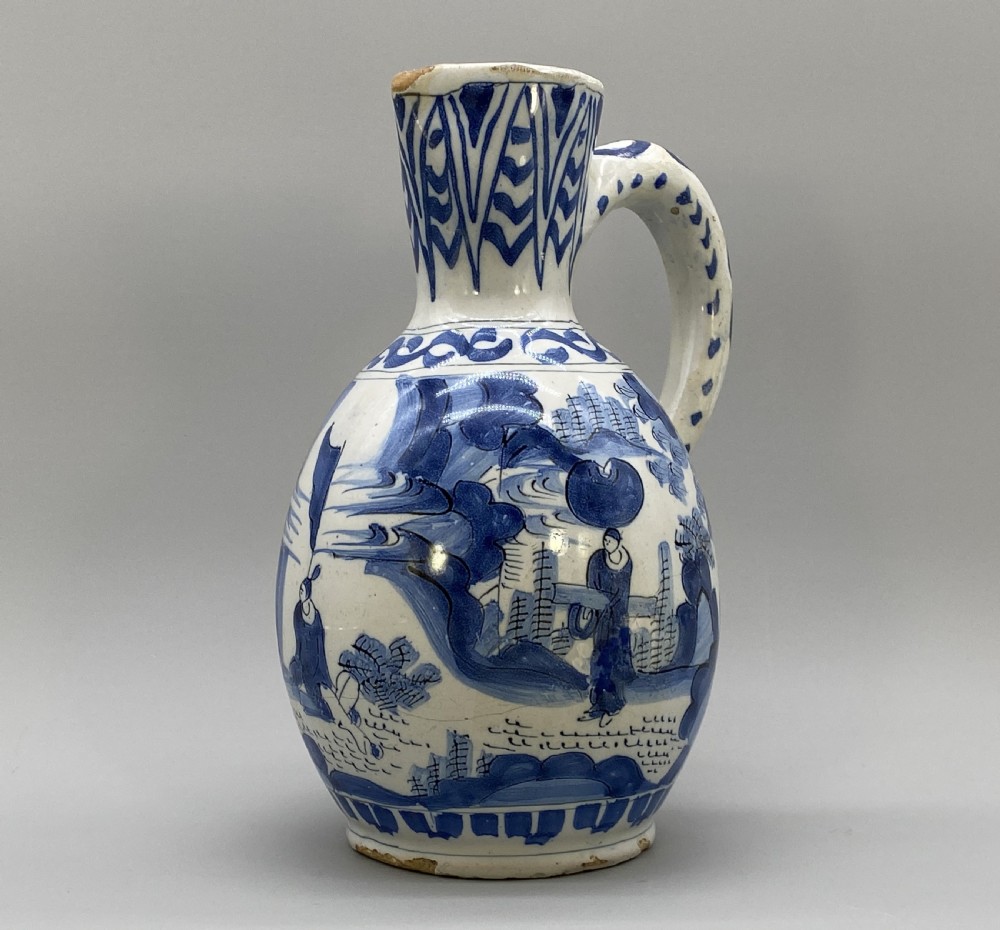 A 17th-century Dutch Delftware ceramic jug featuring hand-painted blue chinoiserie scenes on an opaque white tin glaze with a curved handle. View V
