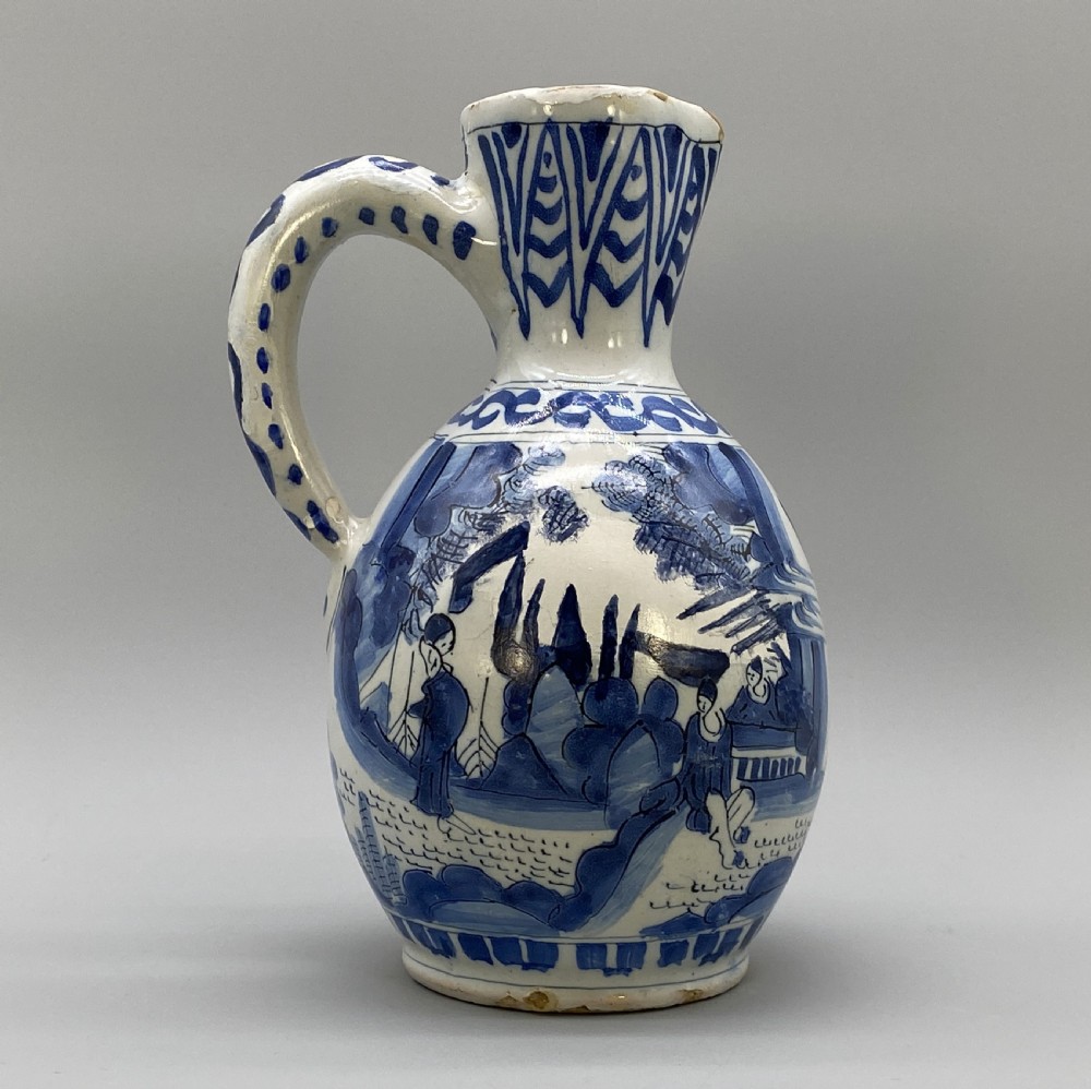 A 17th-century Dutch Delftware ceramic jug featuring hand-painted blue chinoiserie scenes on an opaque white tin glaze with a curved handle. View IX