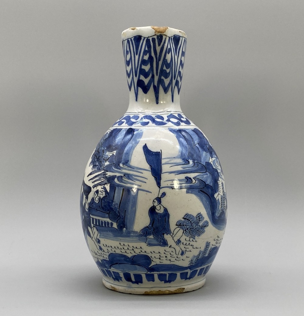 A 17th-century Dutch Delftware ceramic jug featuring hand-painted blue chinoiserie scenes on an opaque white tin glaze with a curved handle. View X