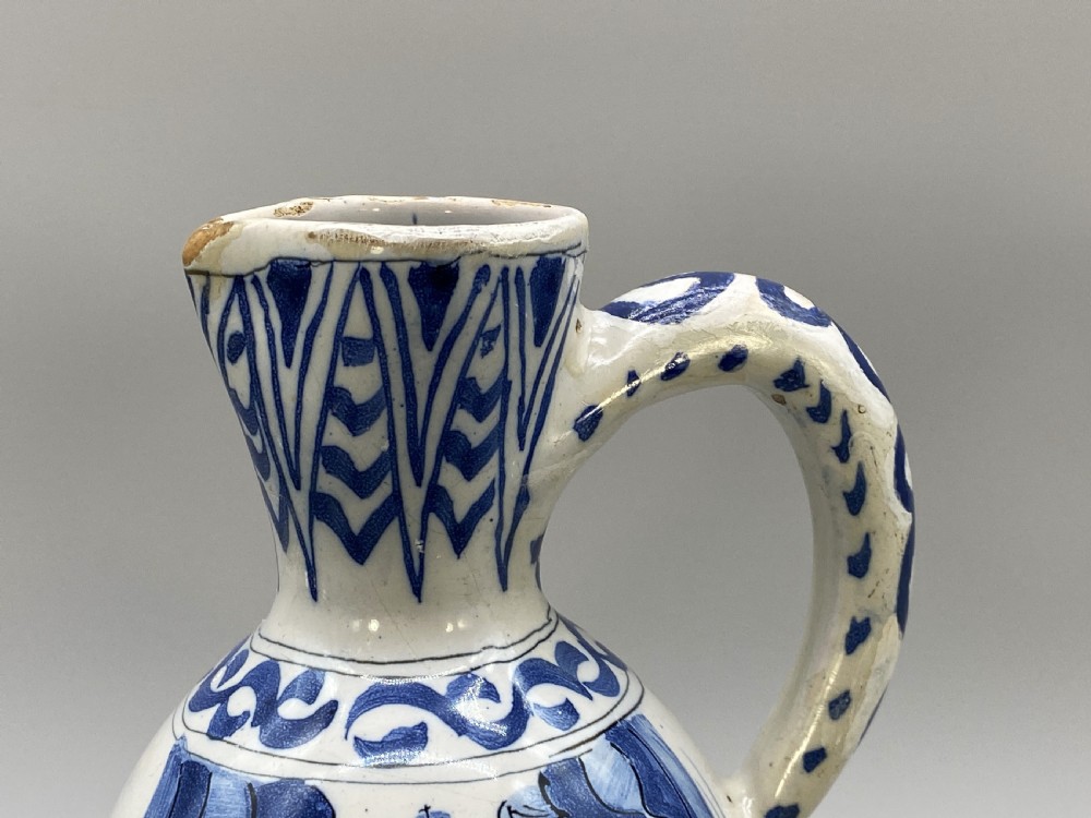 A 17th-century Dutch Delftware ceramic jug featuring hand-painted blue chinoiserie scenes on an opaque white tin glaze with a curved handle. View XIII