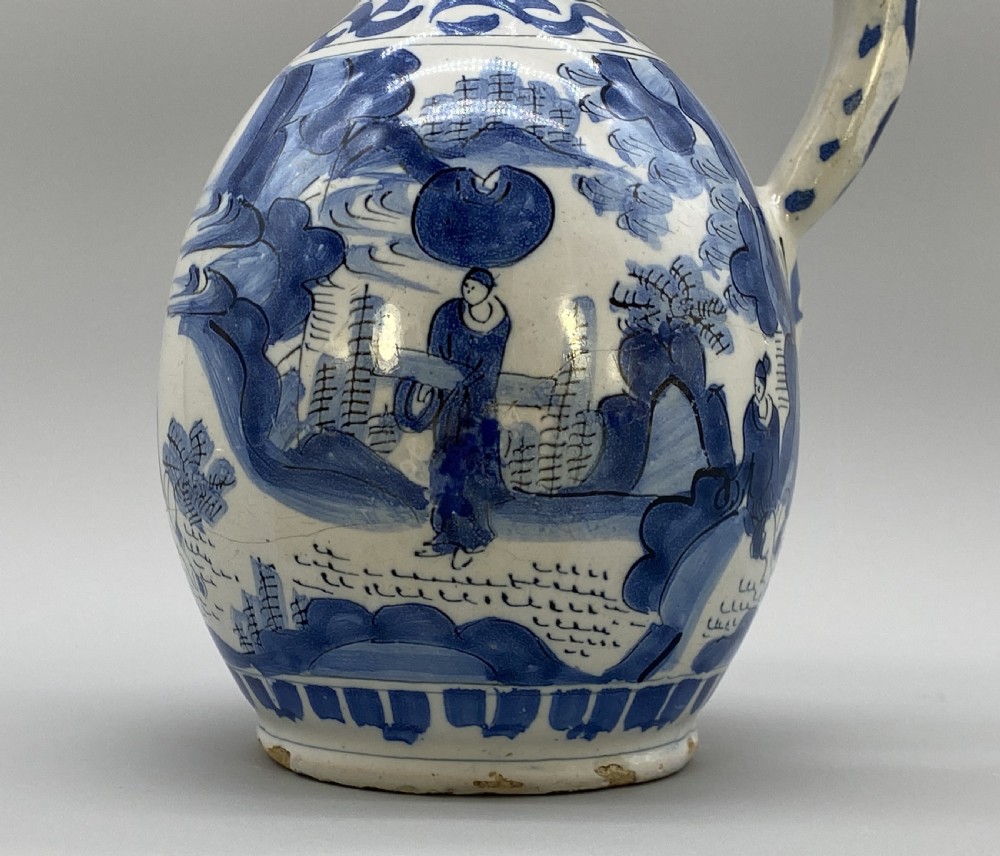 A 17th-century Dutch Delftware ceramic jug featuring hand-painted blue chinoiserie scenes on an opaque white tin glaze with a curved handle. View XIV