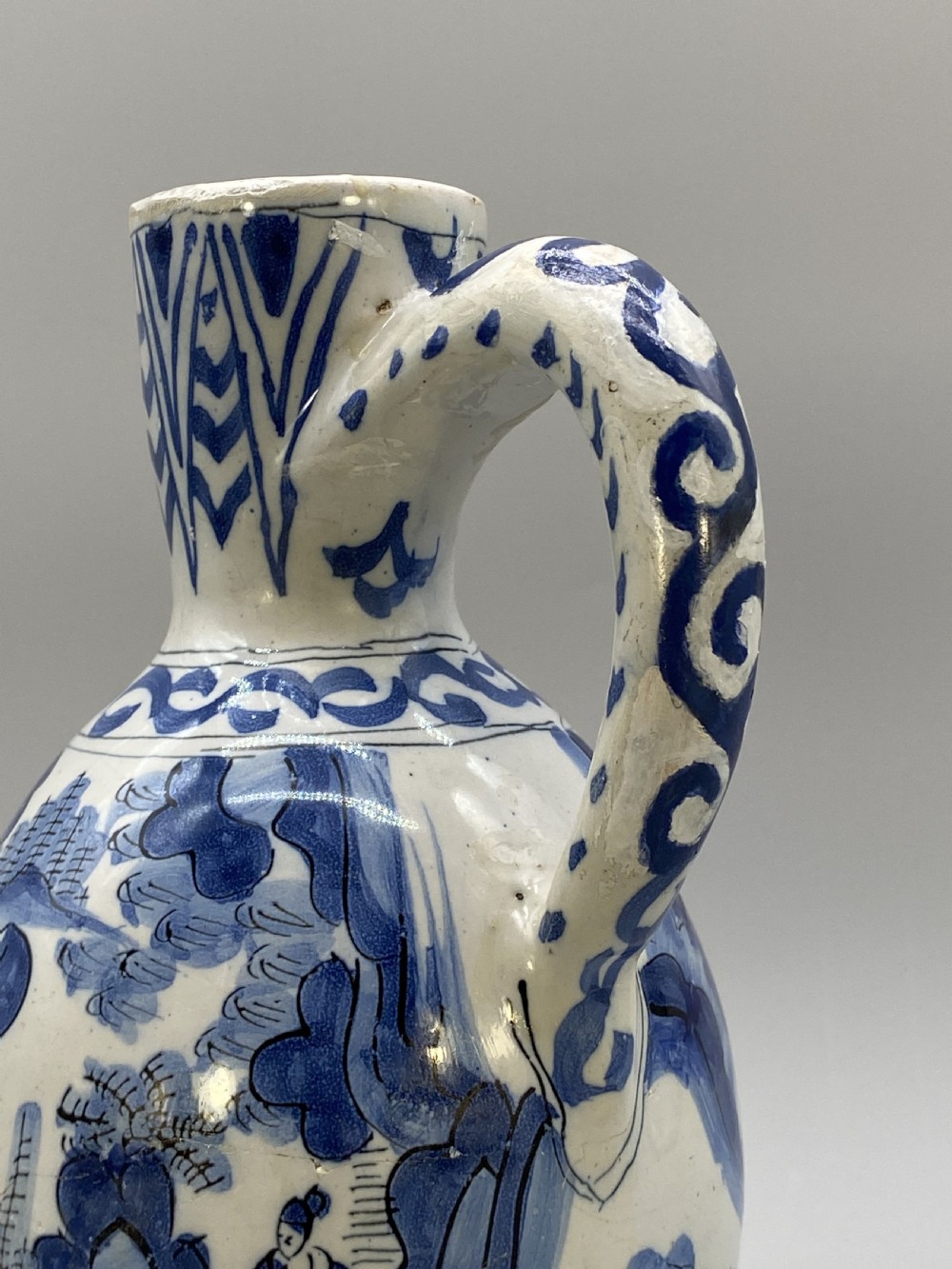 A 17th-century Dutch Delftware ceramic jug featuring hand-painted blue chinoiserie scenes on an opaque white tin glaze with a curved handle. View XV
