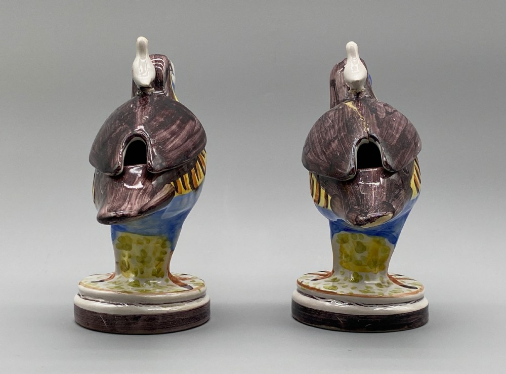 A pair of 18th-century Spanish tin-glazed faience tureens fashioned as partridges with hand-painted blue, yellow, and brown plumage and small bird finials on their removable covers. View X