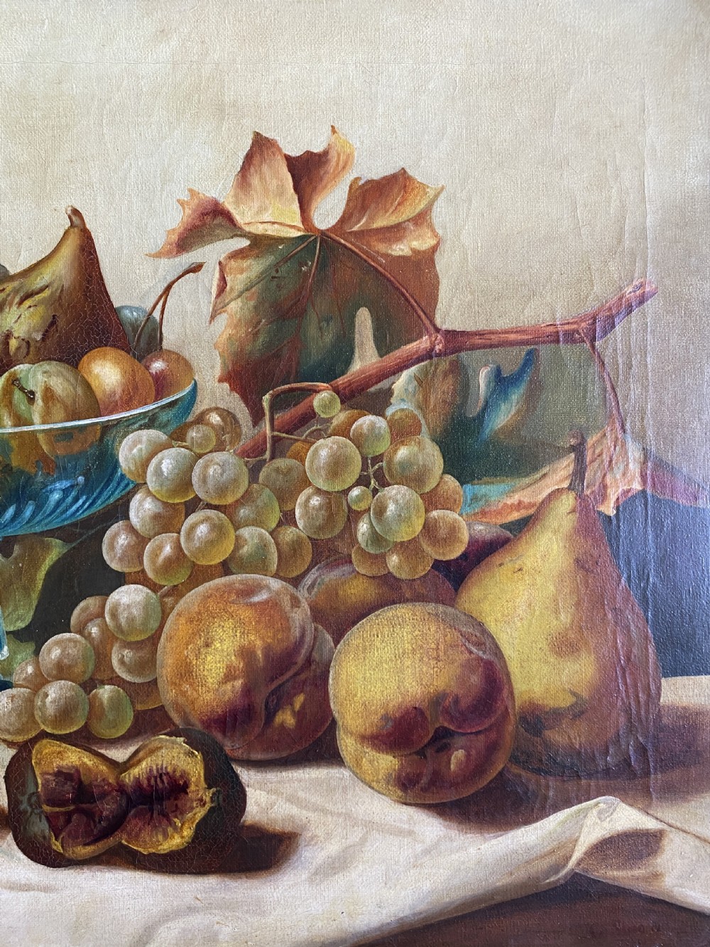 An oil painting depicting a still life composition of grapes, pears, peaches, and figs arranged on a draped cloth with a blue glass pedestal dish, enclosed in a moulded gilt frame. View IV