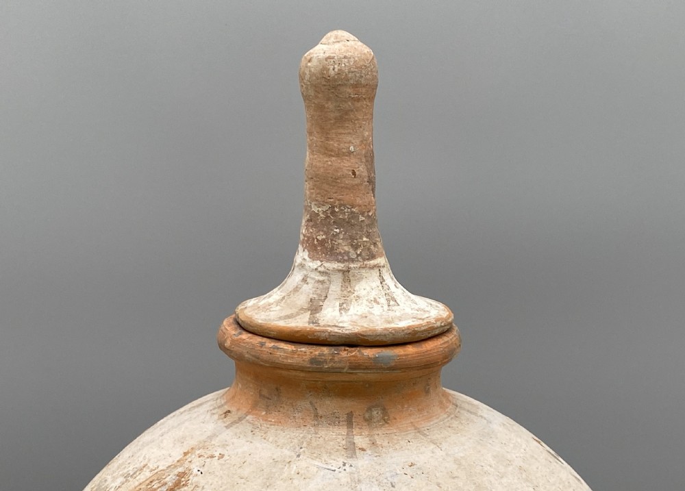 A painted terracotta vessel from the Tang Dynasty featuring a bulbous body, pointed finial lid, flared pedestal foot, and painted geometric scroll motifs in red and grey pigments. View III
