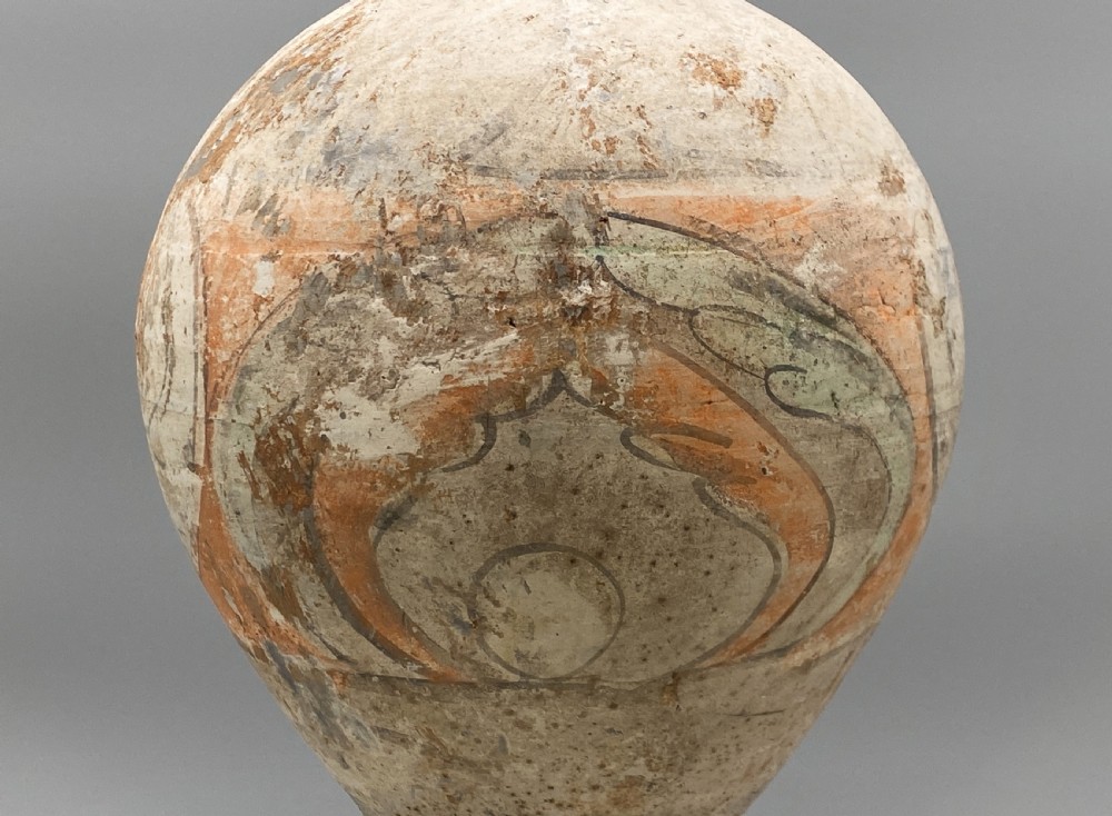 A painted terracotta vessel from the Tang Dynasty featuring a bulbous body, pointed finial lid, flared pedestal foot, and painted geometric scroll motifs in red and grey pigments. View V