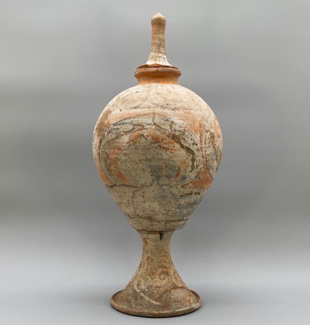 A painted terracotta vessel from the Tang Dynasty featuring a bulbous body, pointed finial lid, flared pedestal foot, and painted geometric scroll motifs in red and grey pigments. View VII