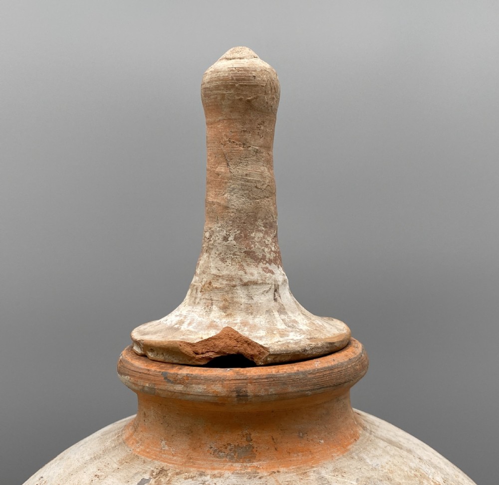 A painted terracotta vessel from the Tang Dynasty featuring a bulbous body, pointed finial lid, flared pedestal foot, and painted geometric scroll motifs in red and grey pigments. View IX