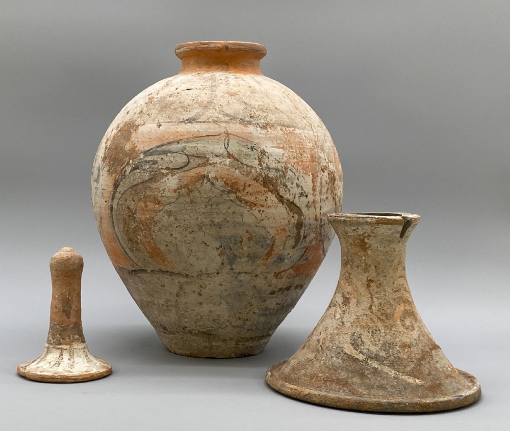 A painted terracotta vessel from the Tang Dynasty featuring a bulbous body, pointed finial lid, flared pedestal foot, and painted geometric scroll motifs in red and grey pigments. View XI