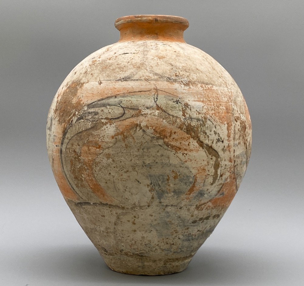 A painted terracotta vessel from the Tang Dynasty featuring a bulbous body, pointed finial lid, flared pedestal foot, and painted geometric scroll motifs in red and grey pigments. View XII