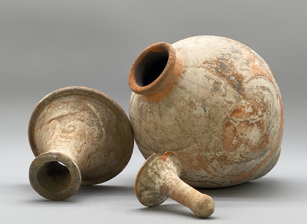 A painted terracotta vessel from the Tang Dynasty featuring a bulbous body, pointed finial lid, flared pedestal foot, and painted geometric scroll motifs in red and grey pigments. View XIX