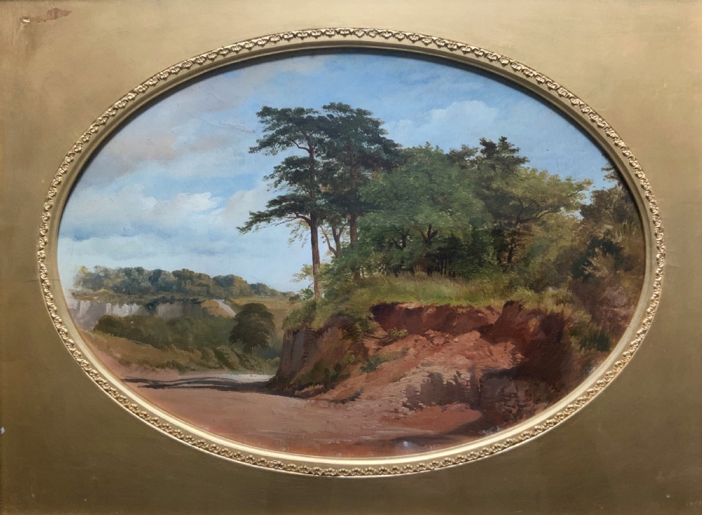 An oval 19th-century oil landscape painting depicting a wooded bank and open fields, set inside a rectangular gilded frame. View II