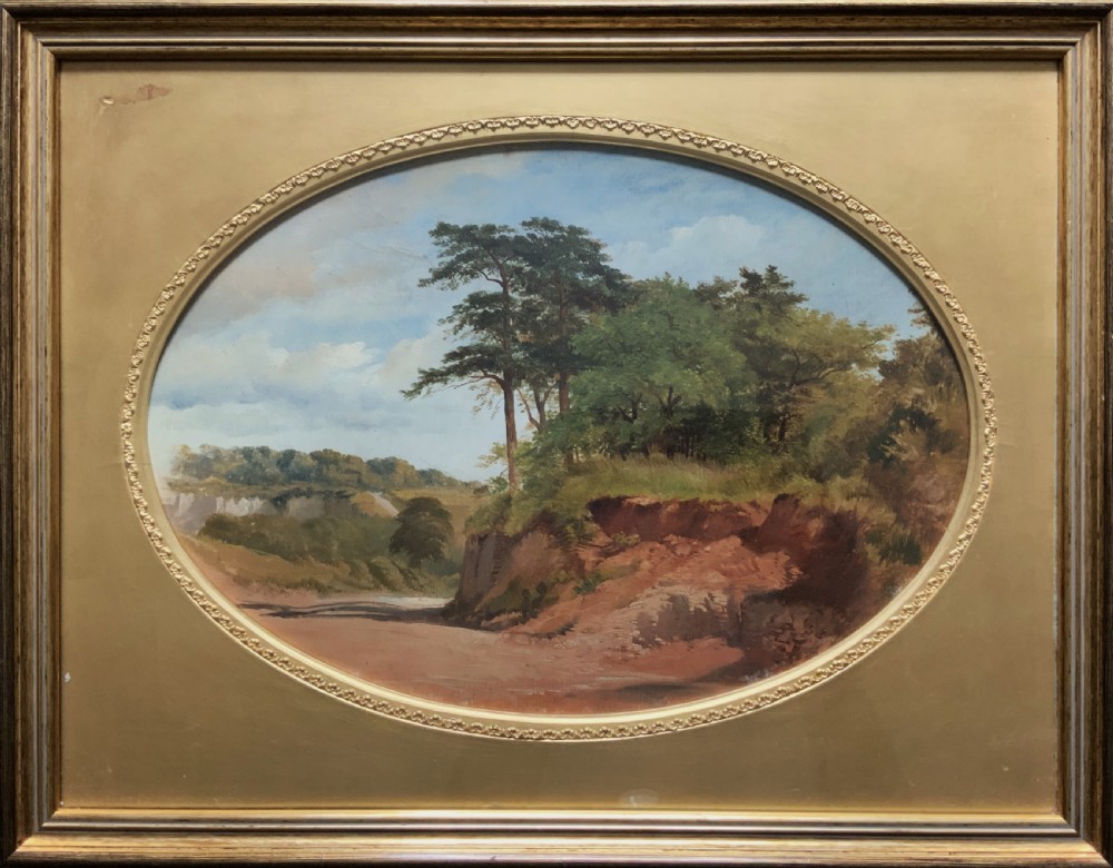 An oval 19th-century oil landscape painting depicting a wooded bank and open fields, set inside a rectangular gilded frame. View X
