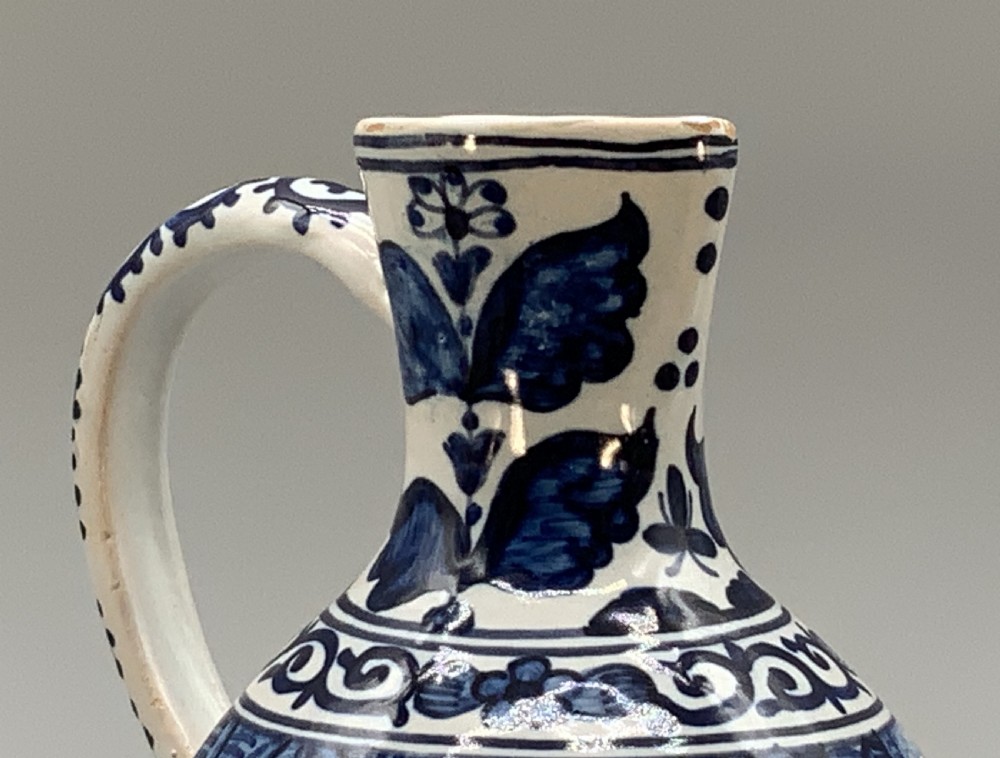 An antique Dutch Delftware ceramic jug decorated with cobalt blue hand-painted Chinoiserie figures and botanical motifs against a white tin glaze. View X