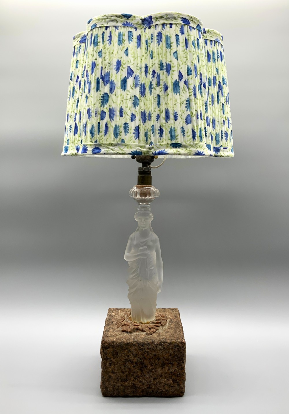 An early 20th-century French table lamp featuring a frosted glass classical figurine mounted on a square stone base, topped with a pleated blue floral lampshade. View VII