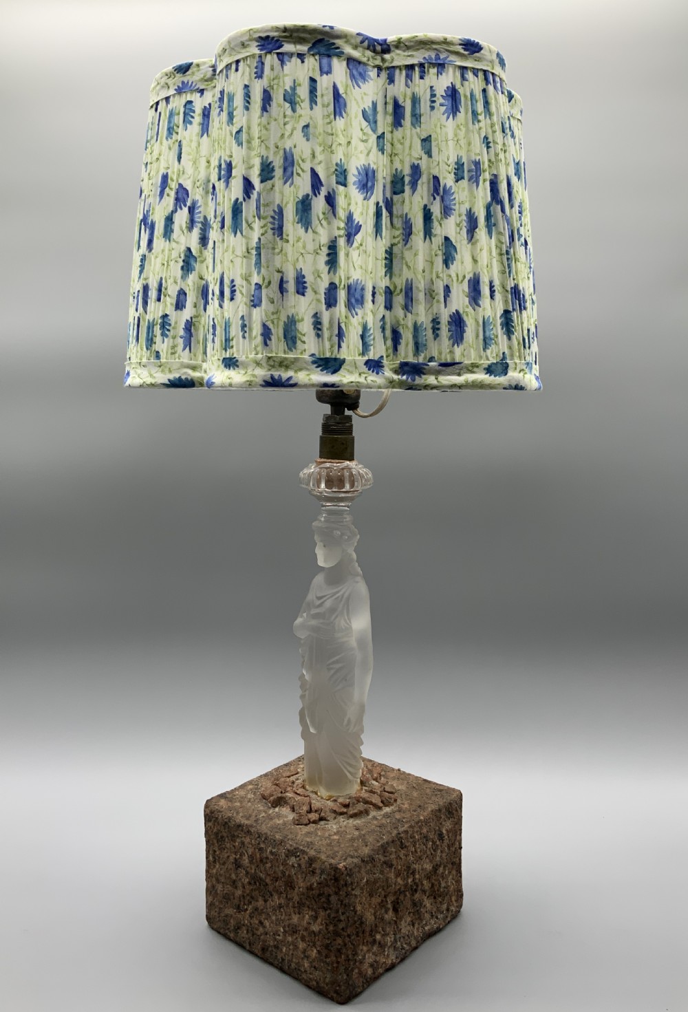 An early 20th-century French table lamp featuring a frosted glass classical figurine mounted on a square stone base, topped with a pleated blue floral lampshade. View VI