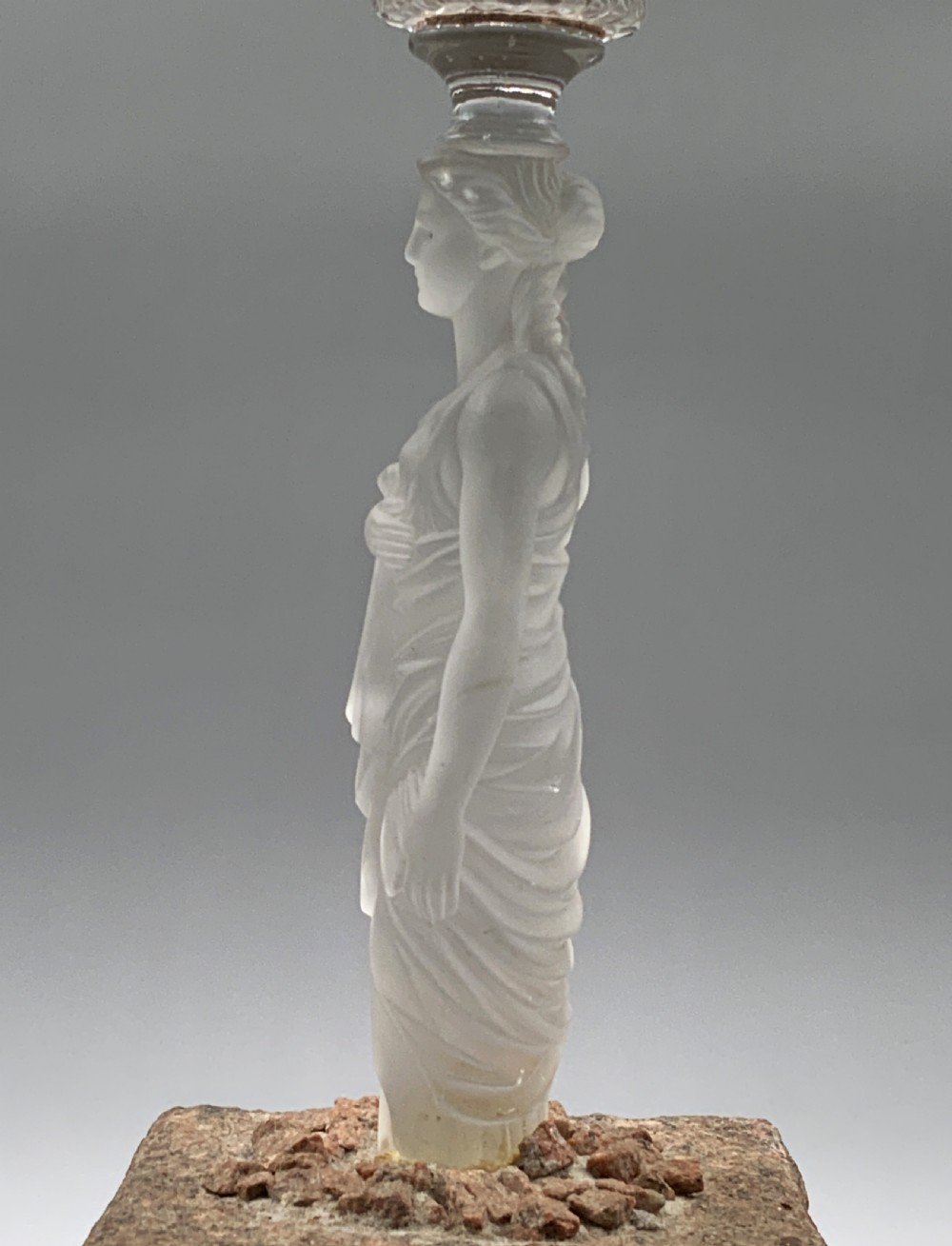 An early 20th-century French table lamp featuring a frosted glass classical figurine mounted on a square stone base, topped with a pleated blue floral lampshade. View X