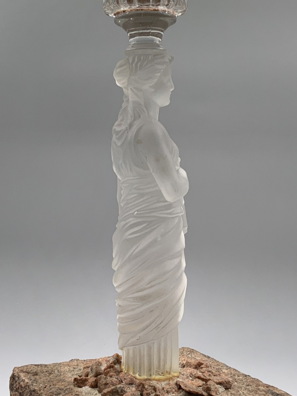 An early 20th-century French table lamp featuring a frosted glass classical figurine mounted on a square stone base, topped with a pleated blue floral lampshade. View XVI