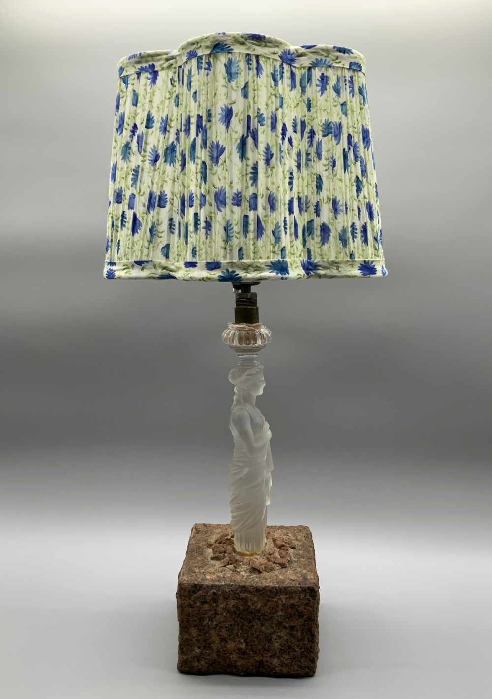 An early 20th-century French table lamp featuring a frosted glass classical figurine mounted on a square stone base, topped with a pleated blue floral lampshade. View XVII