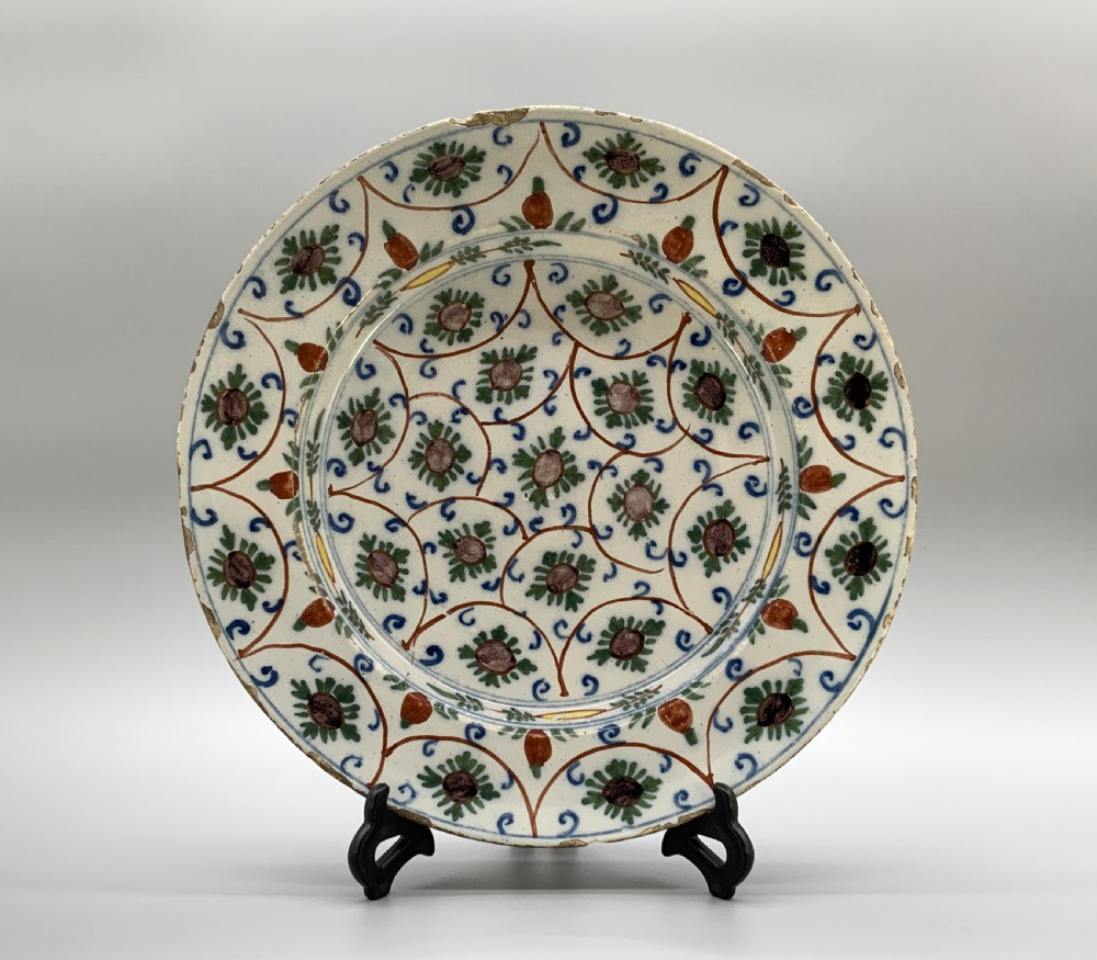 An 18th-century circular Dutch Delftware ceramic charger plate featuring hand-painted green, brown, and blue geometric floral lattice patterns on an off-white tin glaze.