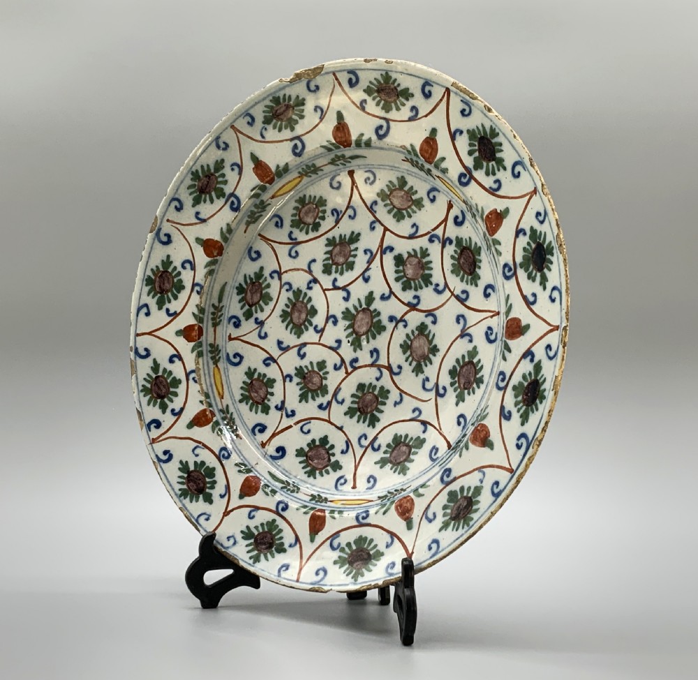 An 18th-century circular Dutch Delftware ceramic charger plate featuring hand-painted green, brown, and blue geometric floral lattice patterns on an off-white tin glaze. View III