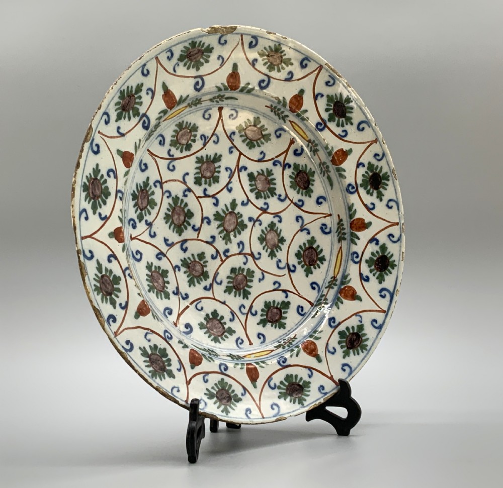 An 18th-century circular Dutch Delftware ceramic charger plate featuring hand-painted green, brown, and blue geometric floral lattice patterns on an off-white tin glaze. View V