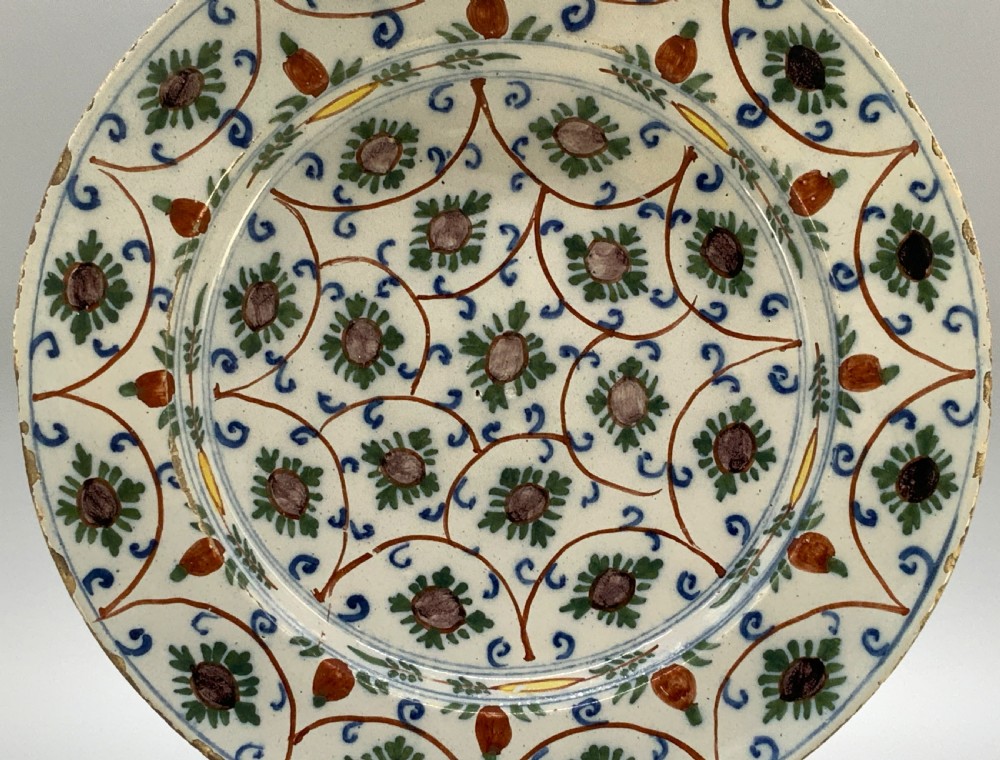 An 18th-century circular Dutch Delftware ceramic charger plate featuring hand-painted green, brown, and blue geometric floral lattice patterns on an off-white tin glaze. View VI