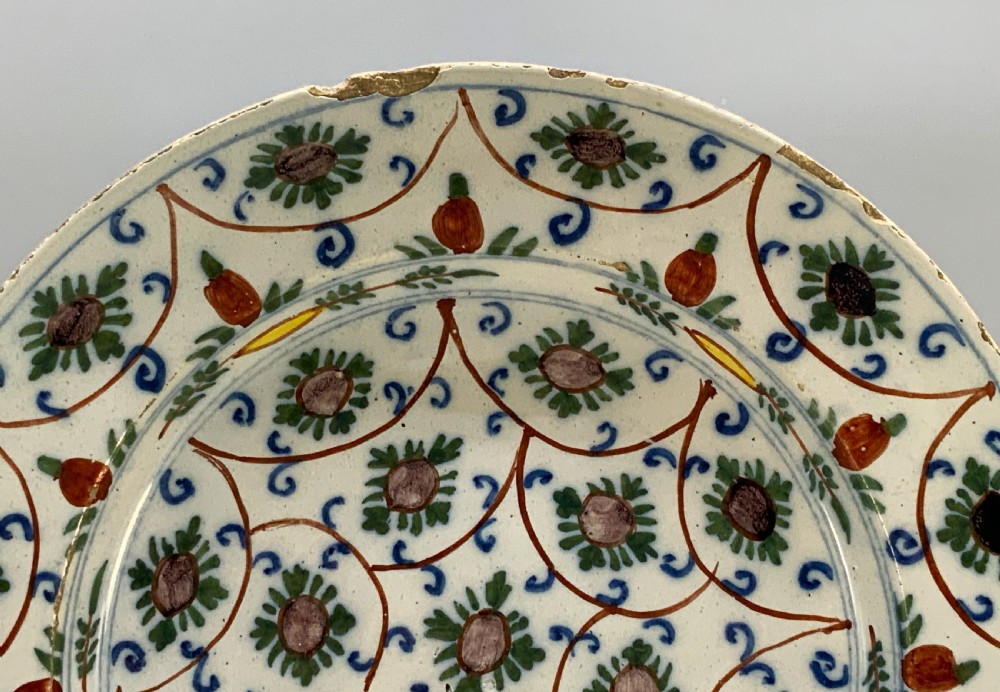 An 18th-century circular Dutch Delftware ceramic charger plate featuring hand-painted green, brown, and blue geometric floral lattice patterns on an off-white tin glaze. View VII