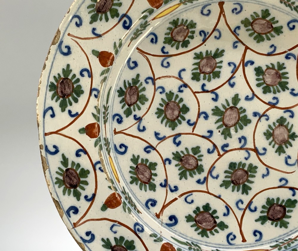 An 18th-century circular Dutch Delftware ceramic charger plate featuring hand-painted green, brown, and blue geometric floral lattice patterns on an off-white tin glaze. View VIII