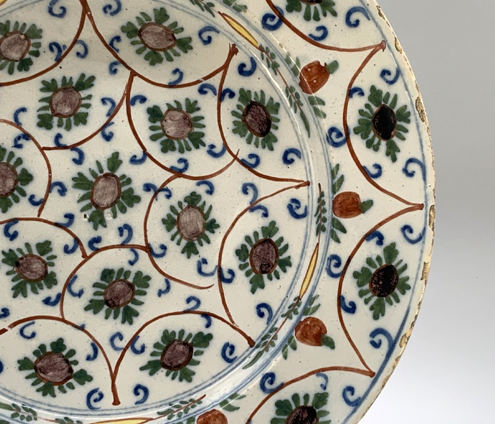 An 18th-century circular Dutch Delftware ceramic charger plate featuring hand-painted green, brown, and blue geometric floral lattice patterns on an off-white tin glaze. View IX