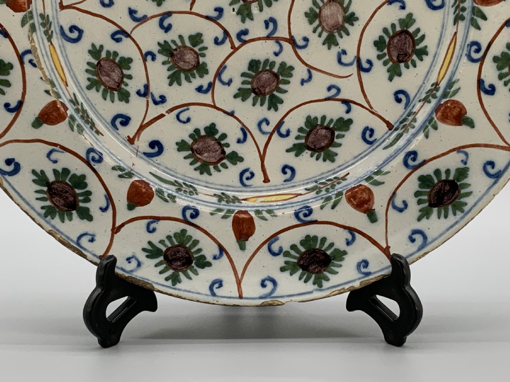 An 18th-century circular Dutch Delftware ceramic charger plate featuring hand-painted green, brown, and blue geometric floral lattice patterns on an off-white tin glaze. View X