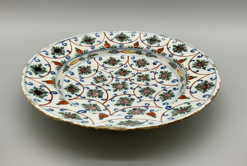 An 18th-century circular Dutch Delftware ceramic charger plate featuring hand-painted green, brown, and blue geometric floral lattice patterns on an off-white tin glaze. View XII