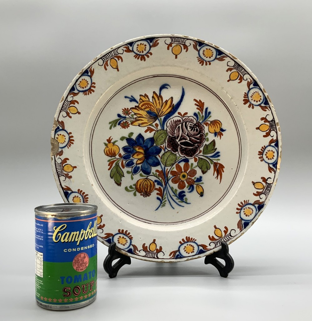 An 18th-century circular tin-glazed earthenware charger plate decorated with hand-painted floral motifs in manganese purple, cobalt blue, ochre yellow, and green. View II