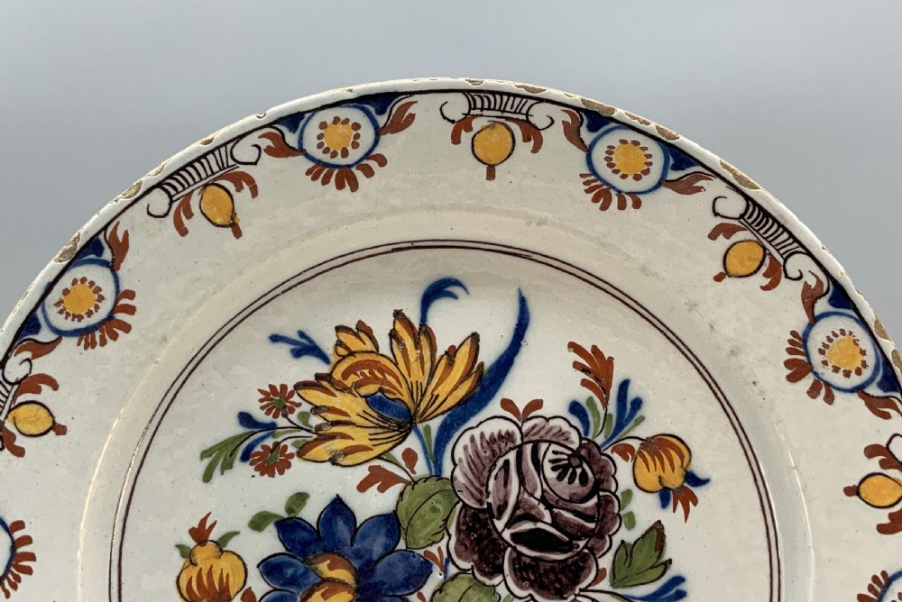 An 18th-century circular tin-glazed earthenware charger plate decorated with hand-painted floral motifs in manganese purple, cobalt blue, ochre yellow, and green. View V
