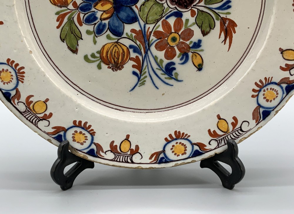 An 18th-century circular tin-glazed earthenware charger plate decorated with hand-painted floral motifs in manganese purple, cobalt blue, ochre yellow, and green. View VI