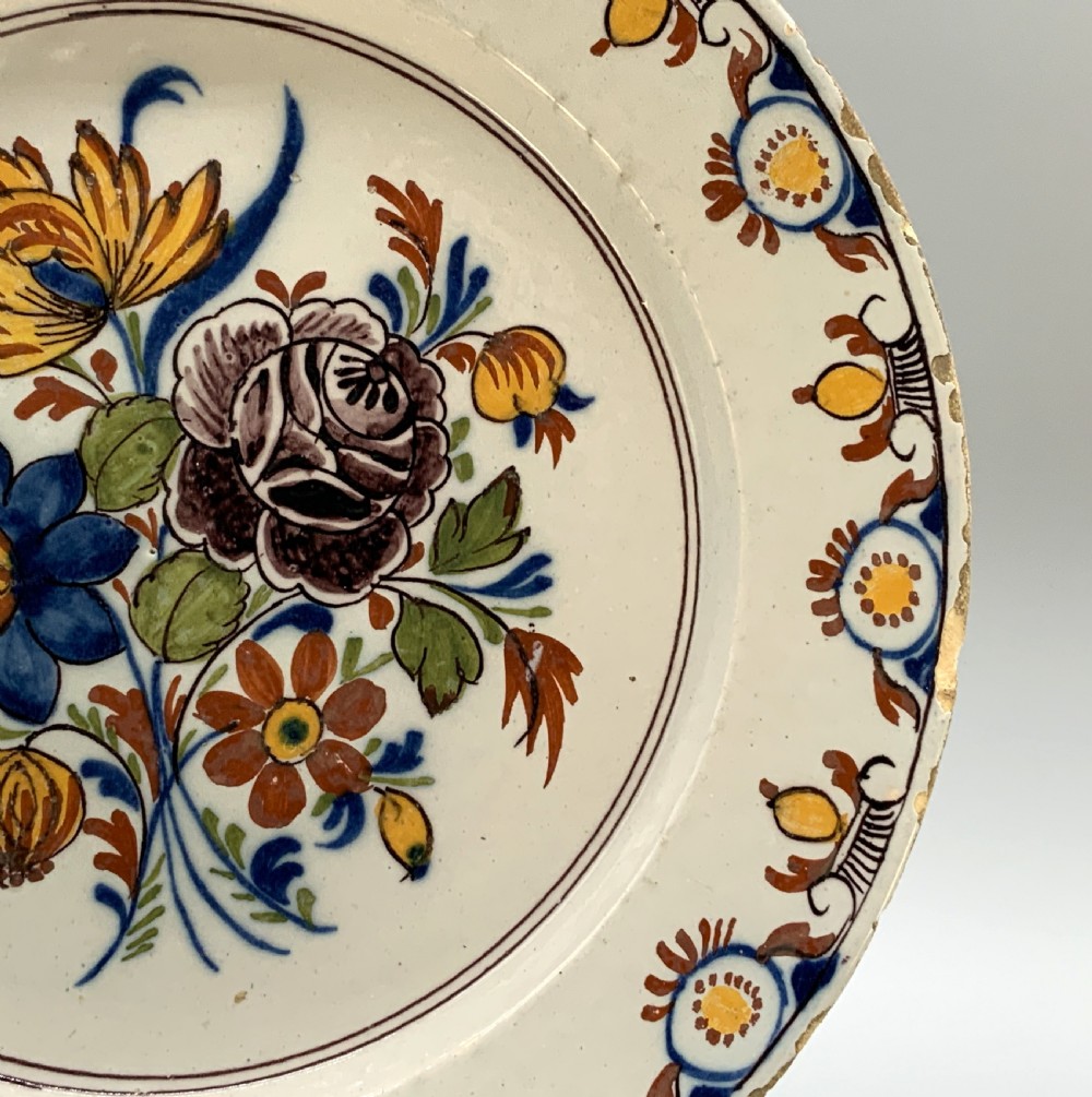 An 18th-century circular tin-glazed earthenware charger plate decorated with hand-painted floral motifs in manganese purple, cobalt blue, ochre yellow, and green. View VIII