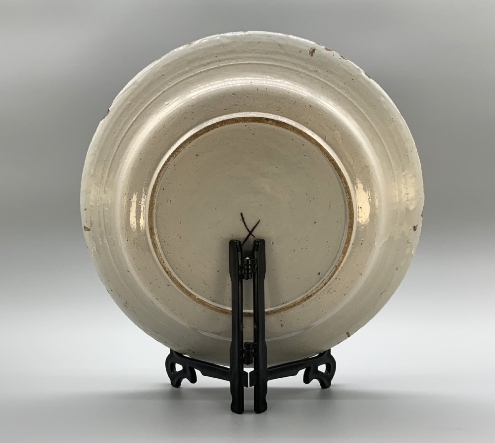 An 18th-century circular tin-glazed earthenware charger plate decorated with hand-painted floral motifs in manganese purple, cobalt blue, ochre yellow, and green. View XIV