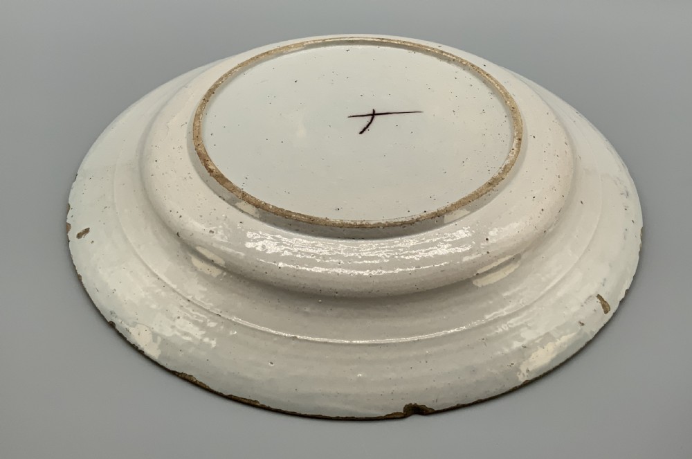 An 18th-century circular tin-glazed earthenware charger plate decorated with hand-painted floral motifs in manganese purple, cobalt blue, ochre yellow, and green. View XVI